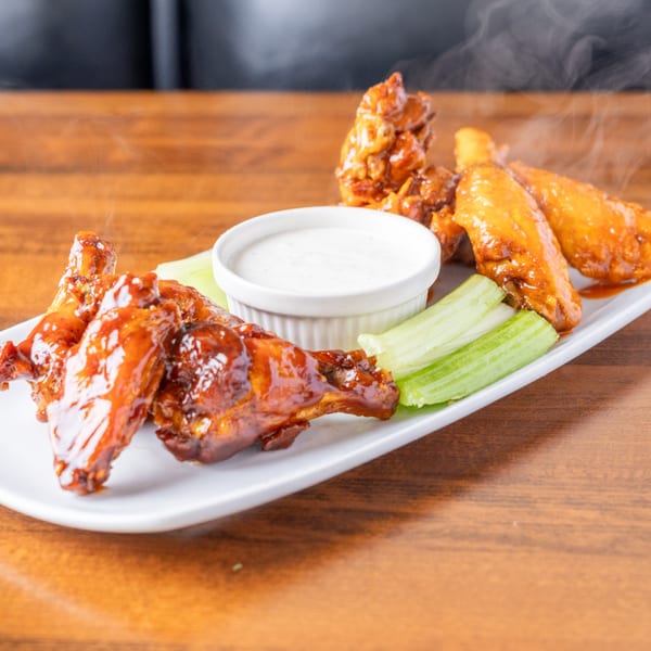 Steaming hot Borinquen Restaurant & Pizzeria chicken wings with ranch dressing and celery sticks on a white plate.