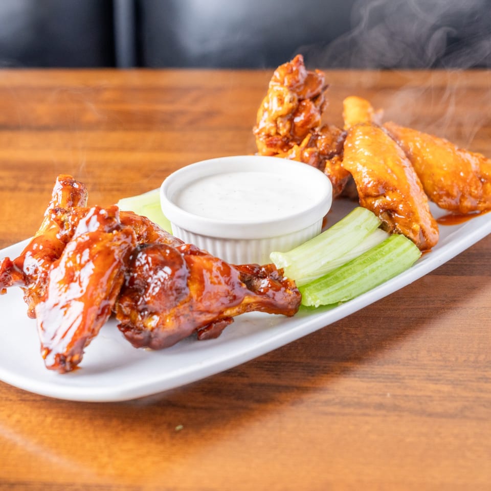 Steaming hot Borinquen Restaurant & Pizzeria chicken wings with ranch dressing and celery sticks on a white plate.