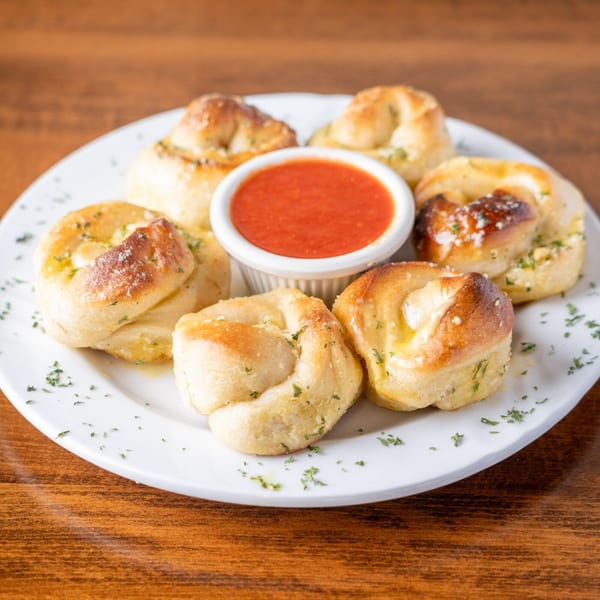 Garlic knots with parsley and Parmesan cheese, served with a side of marinara sauce.