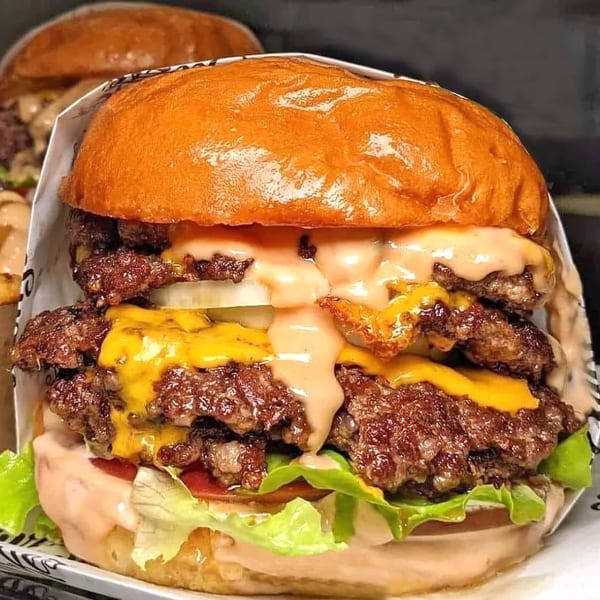 A large double cheeseburger with melted cheese, onions, lettuce, tomato, and sauce on a bun.