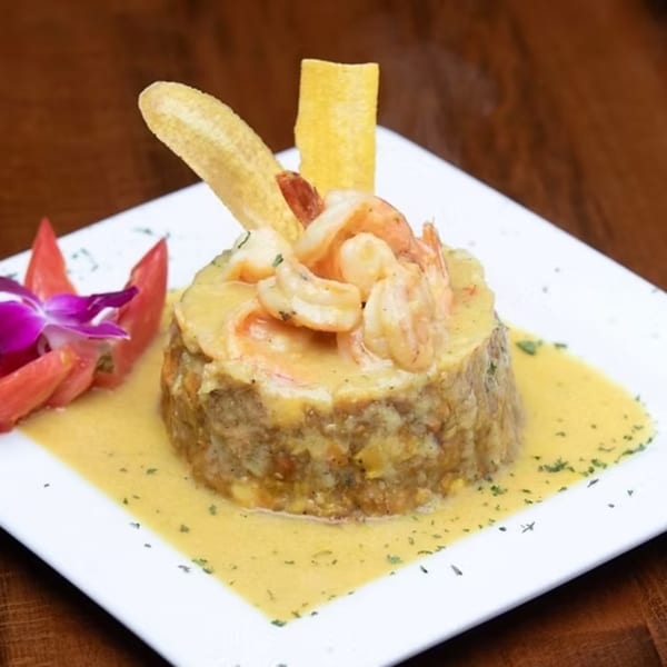 Mofongo with shrimp in a creamy sauce, garnished with plantain chips, tomato, and an orchid.