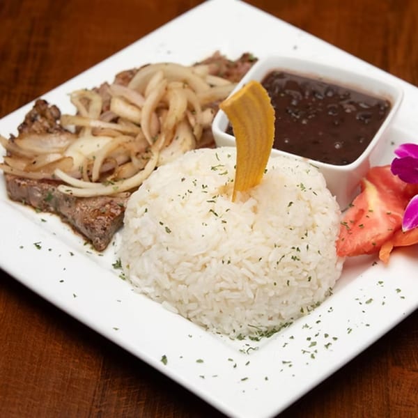 Puerto Rican steak with onions, white rice, black beans, tomatoes, and a plantain chip.