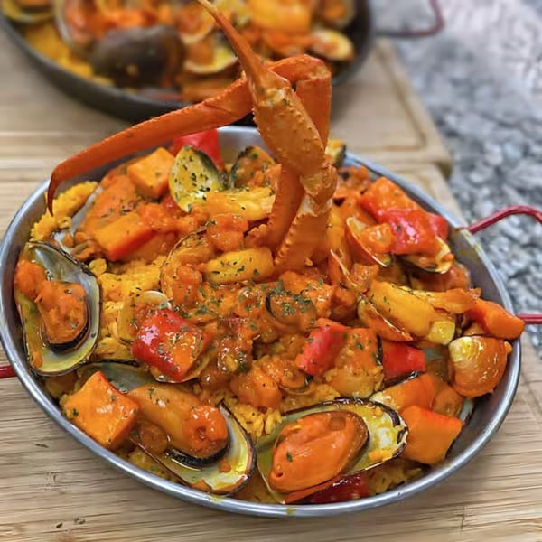 A large paella dish with rice, mussels, crab legs, shrimp, and vegetables.