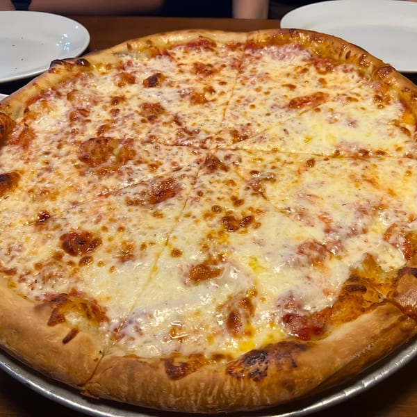 A large, freshly baked cheese pizza with a golden crust, sliced into eight pieces on a metal tray.