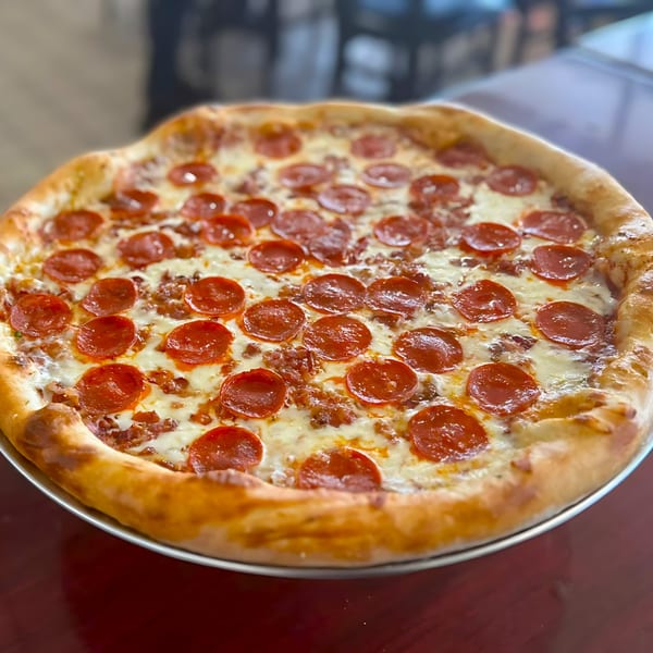 A large, hot pepperoni and sausage pizza with melted cheese on a metal pan.