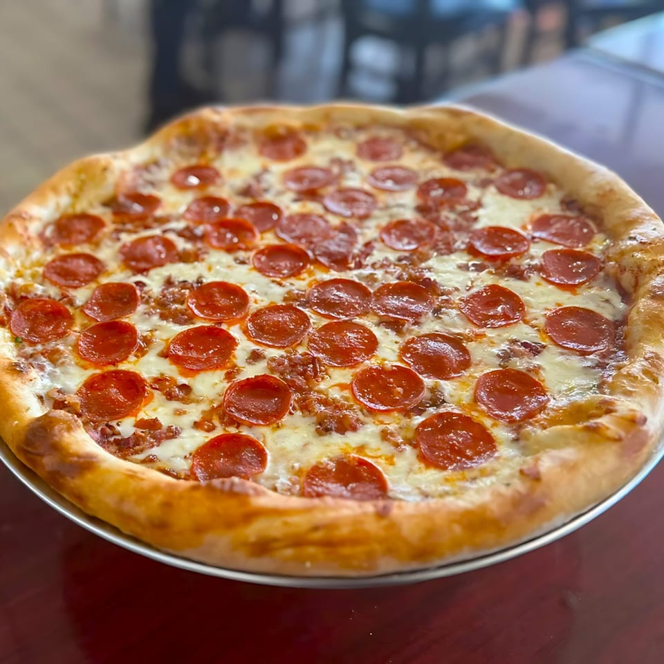A large, hot pepperoni and sausage pizza with melted cheese on a metal pan.